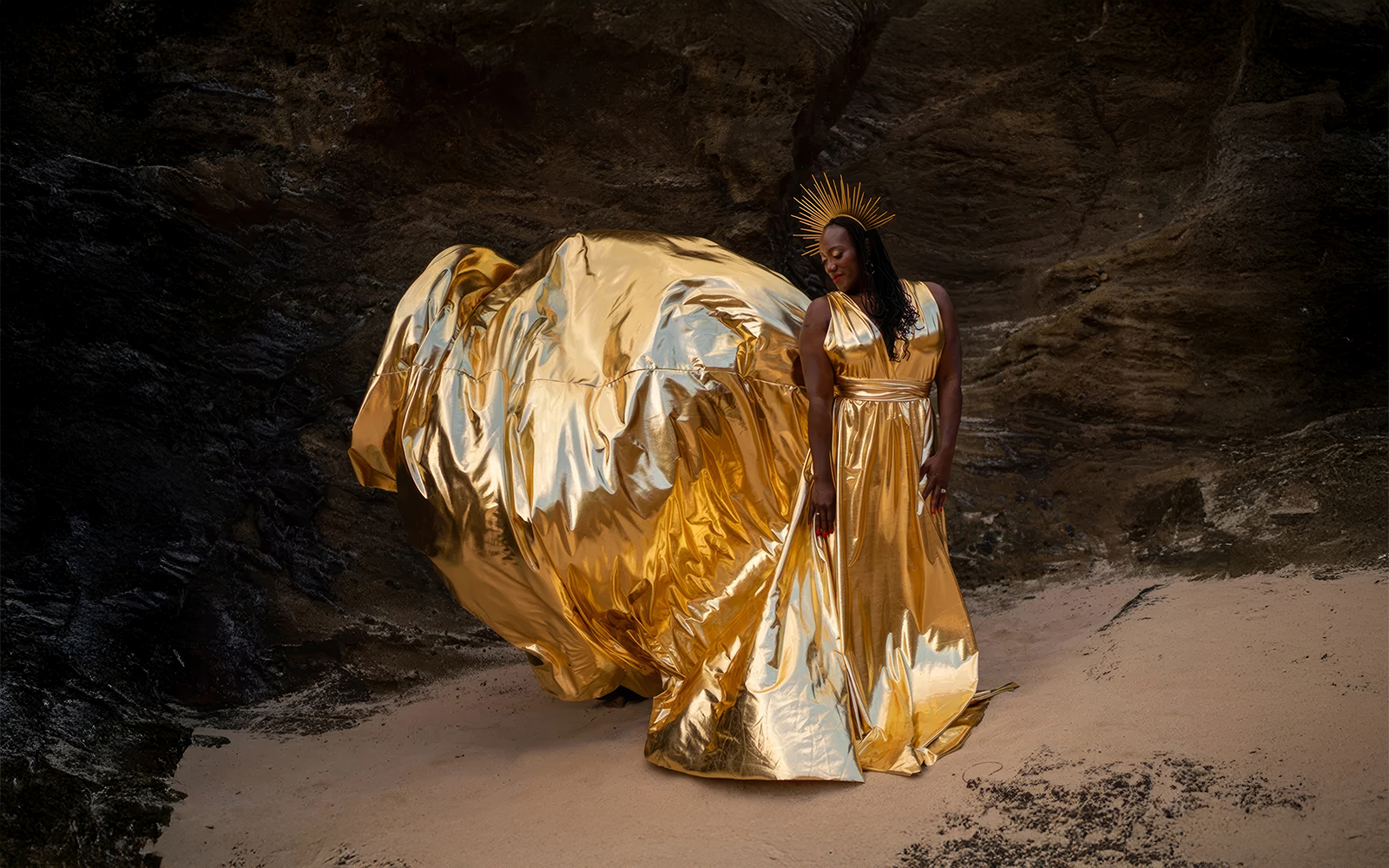 Woman in a gold metallic flying dress inside a sea cave