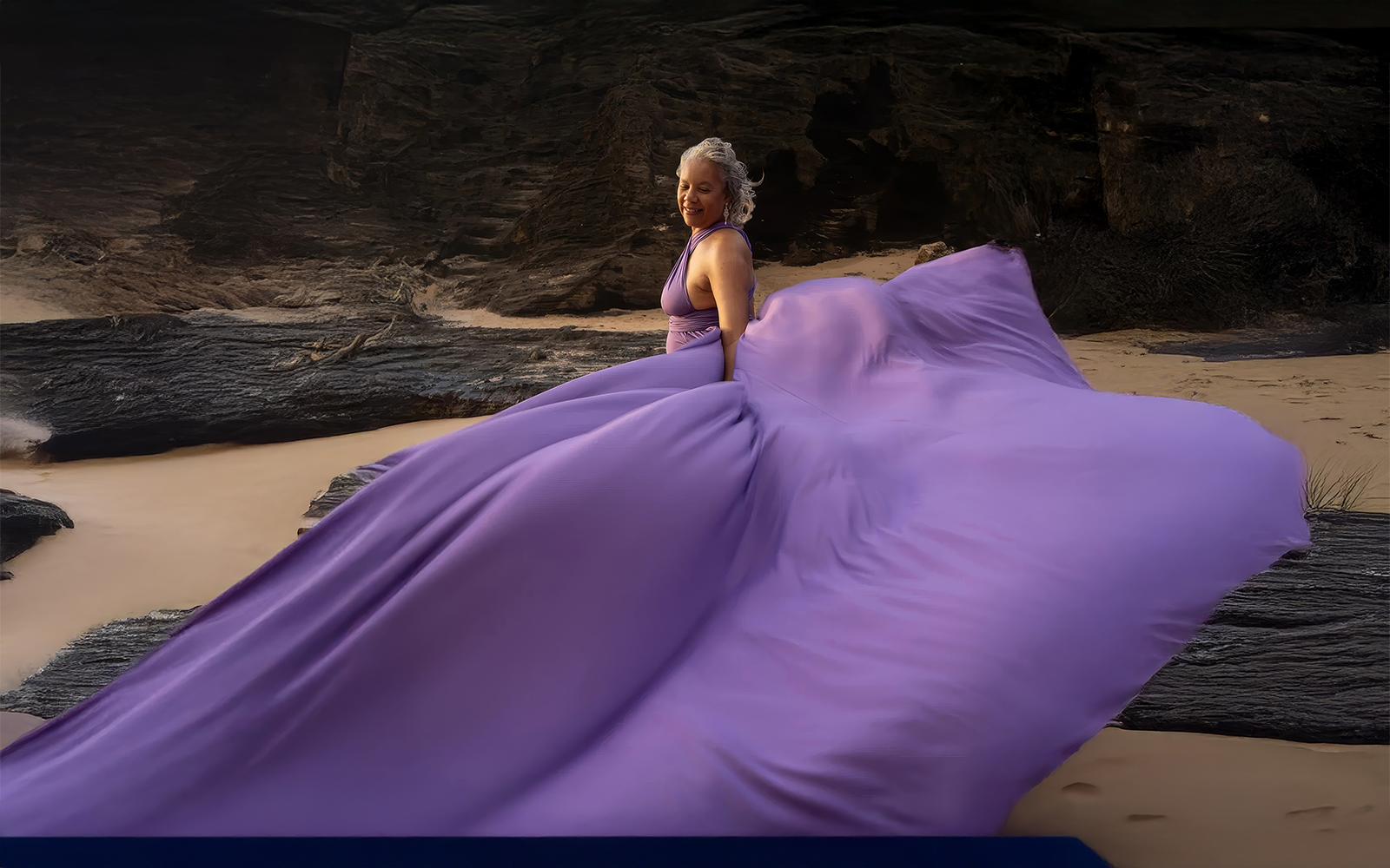 Woman in an orchid lavender flying dress seated beneath coastal cliffs