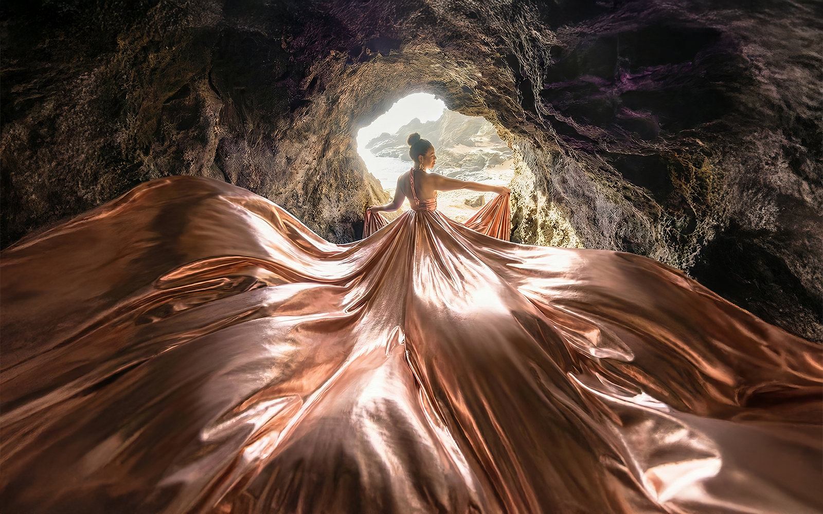 Woman in a rose gold metallic flying dress inside a sea cave