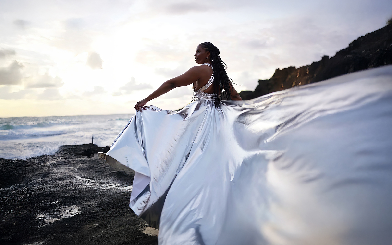 Woman in a silver flying dress on coastal rocks