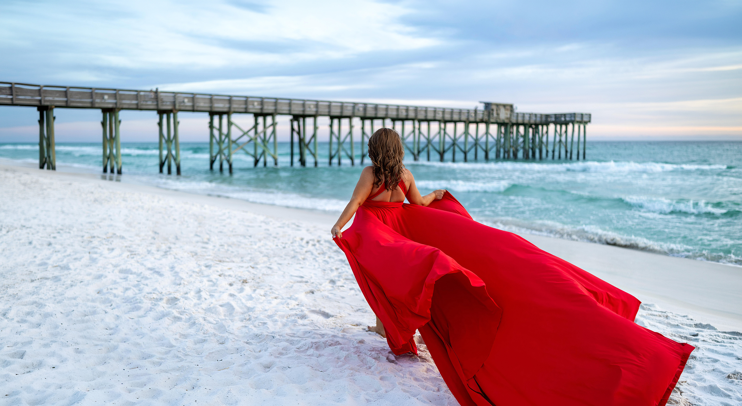PCBpier_wide Woman in a red flying dress on the sand facing the Panama City Beach pier