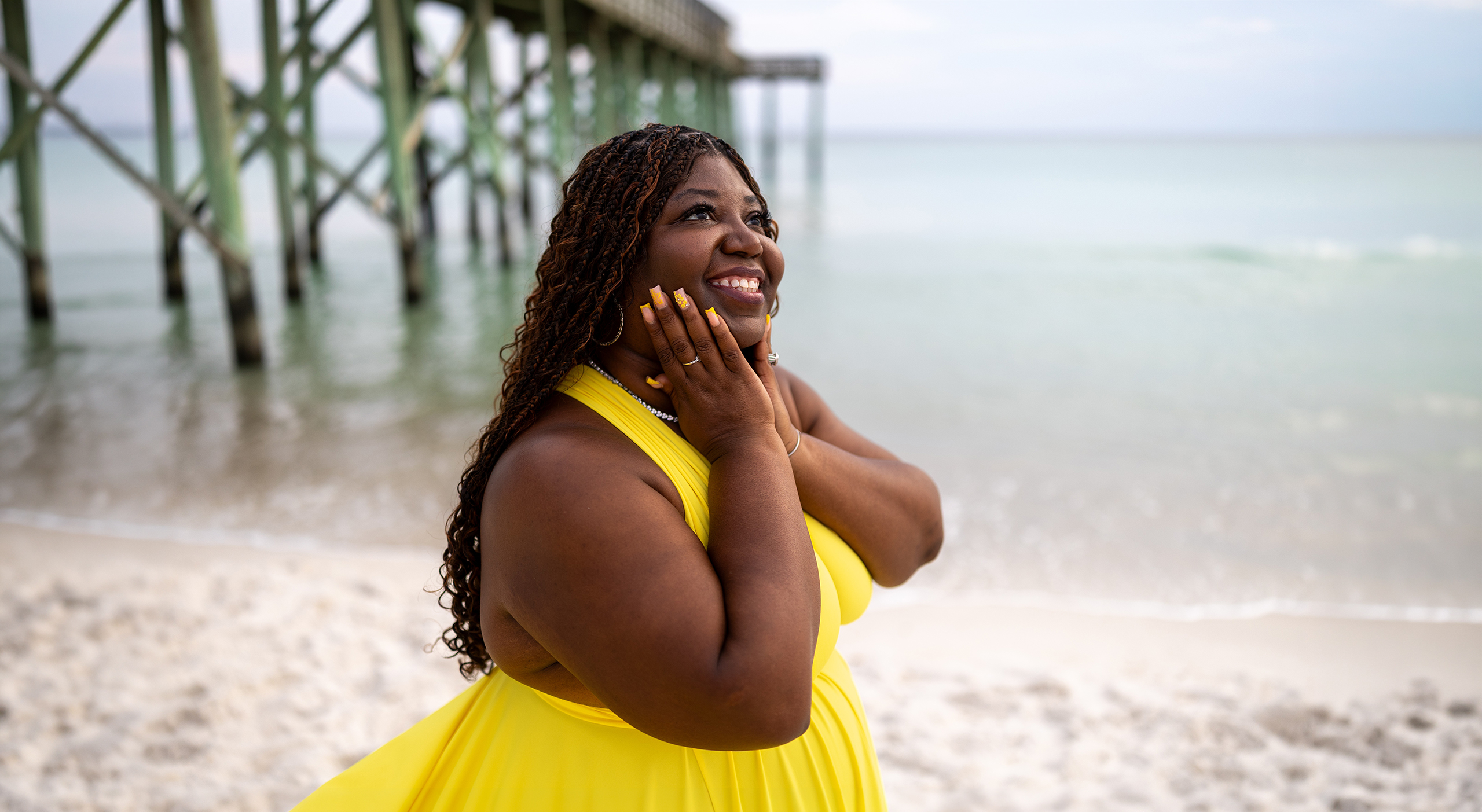 Pier_wide Smiling woman in a yellow flying dress under a beach pier