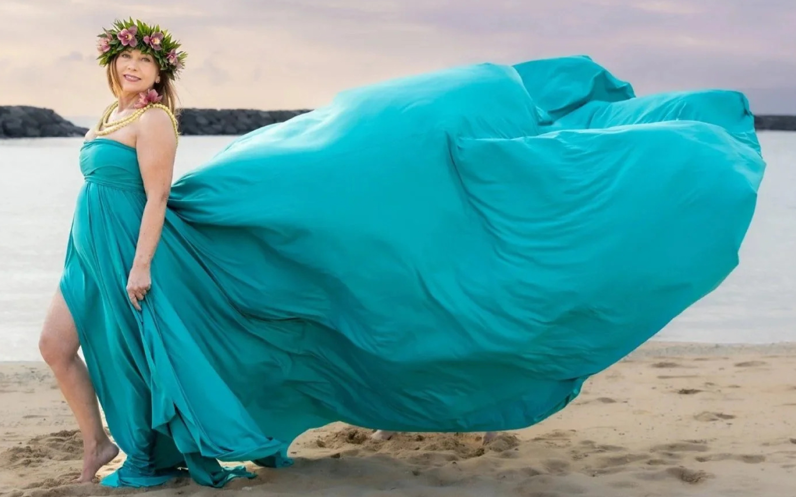 Woman in a teal flying dress billowing in the wind on a beach