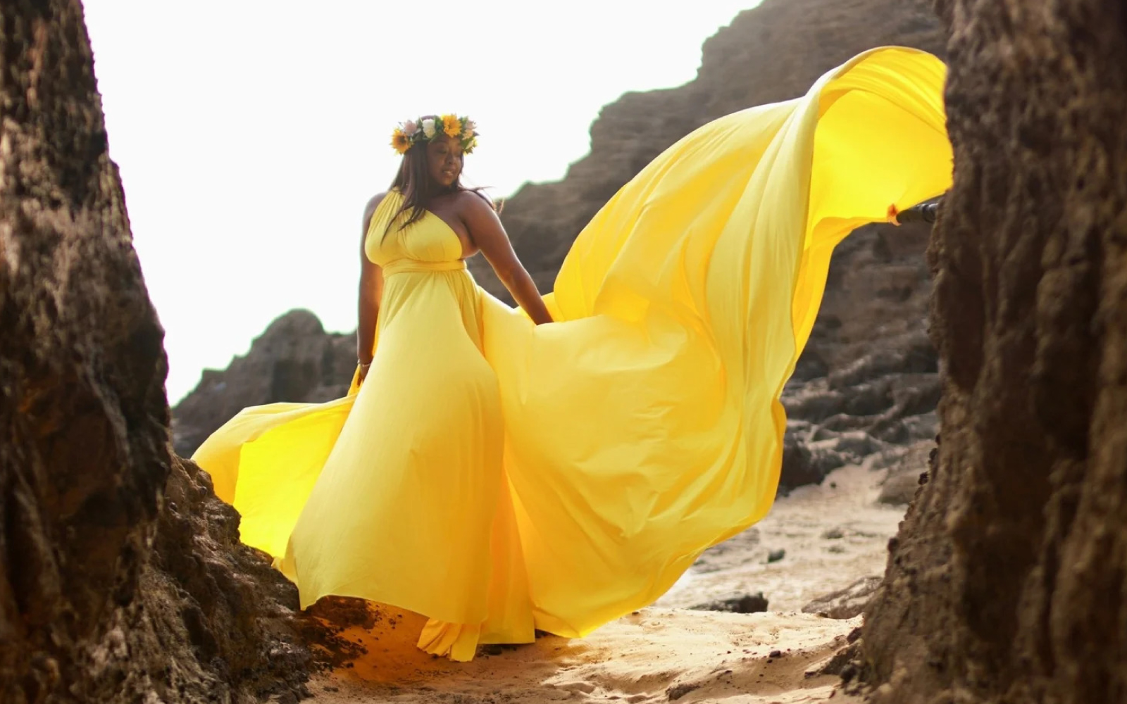 Woman in a yellow flying dress between rock walls on a beach